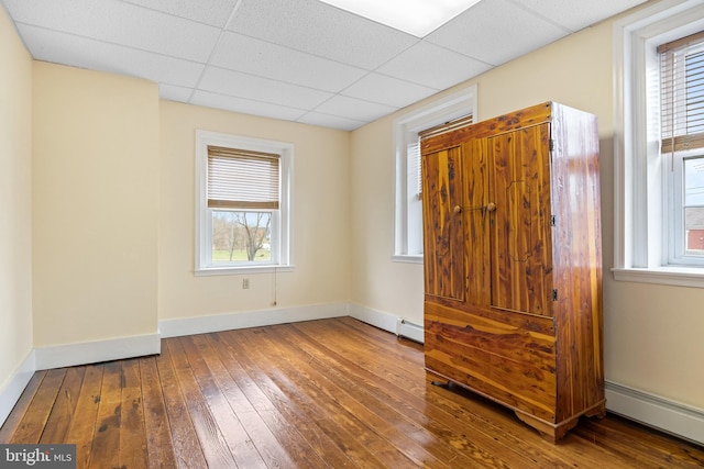 unfurnished bedroom featuring a drop ceiling, wood-type flooring, and a baseboard heating unit