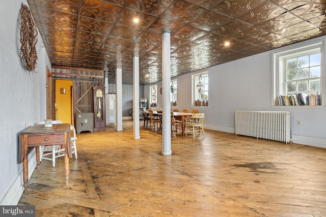 basement featuring a barn door, wood-type flooring, and radiator heating unit