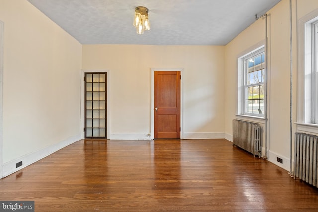 empty room featuring hardwood / wood-style floors, a textured ceiling, and radiator