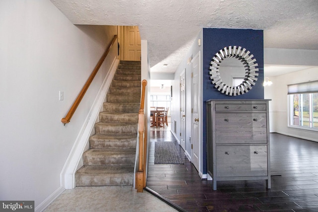 staircase with hardwood / wood-style floors, a textured ceiling, and an inviting chandelier