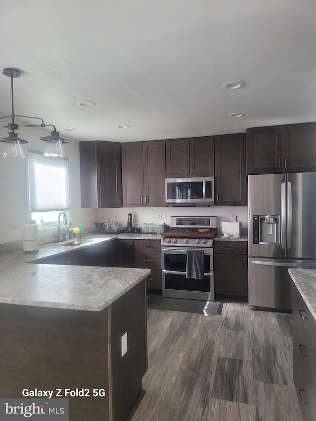 kitchen featuring kitchen peninsula, dark brown cabinetry, stainless steel appliances, sink, and decorative light fixtures