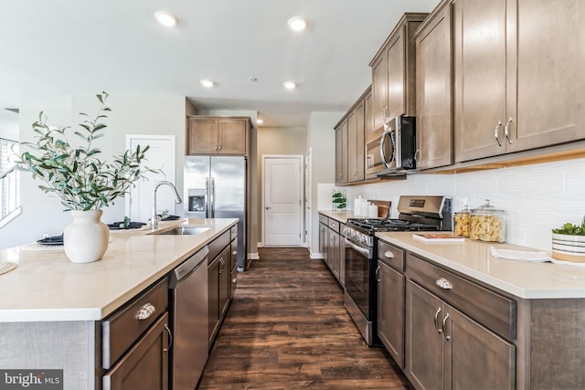 kitchen with a center island with sink, backsplash, appliances with stainless steel finishes, dark hardwood / wood-style floors, and sink