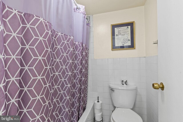 full bath with tile walls, toilet, and a wainscoted wall