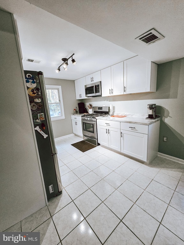 kitchen with stainless steel appliances, light tile patterned flooring, white cabinetry, track lighting, and a textured ceiling