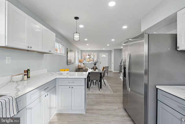 kitchen with kitchen peninsula, stainless steel fridge with ice dispenser, decorative light fixtures, light wood-type flooring, and light stone counters