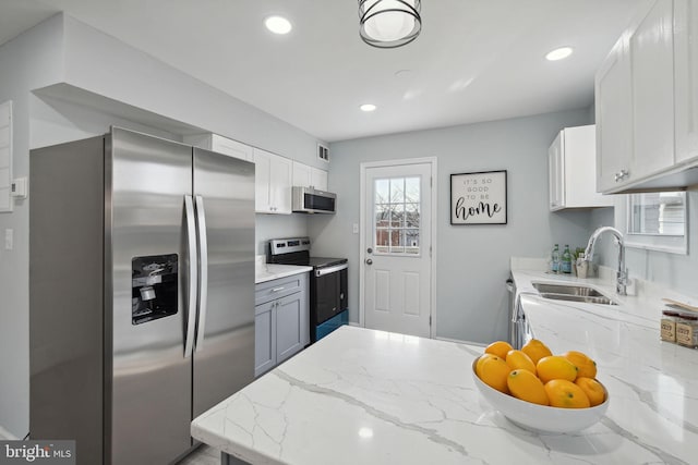 kitchen with white cabinetry, stainless steel appliances, sink, and light stone counters