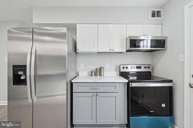 kitchen featuring hardwood / wood-style floors, light stone countertops, stainless steel appliances, and white cabinets