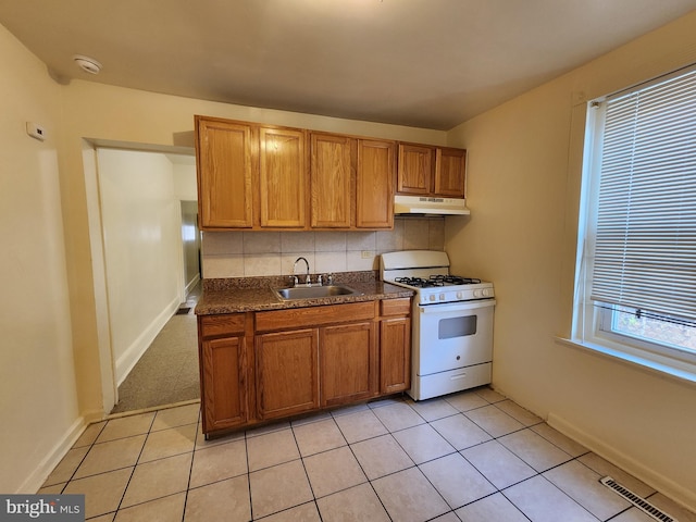 kitchen with light tile patterned flooring, white range with gas cooktop, sink, and backsplash