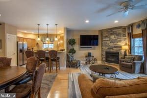 living room featuring a stone fireplace, ceiling fan with notable chandelier, and light hardwood / wood-style floors