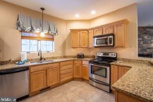 kitchen with appliances with stainless steel finishes, light stone countertops, light brown cabinetry, pendant lighting, and sink