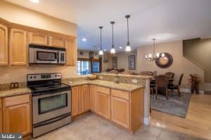 kitchen featuring kitchen peninsula, hanging light fixtures, light wood-type flooring, a notable chandelier, and stainless steel appliances