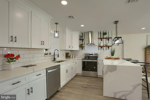 kitchen with wall chimney exhaust hood, white cabinets, stainless steel appliances, and sink