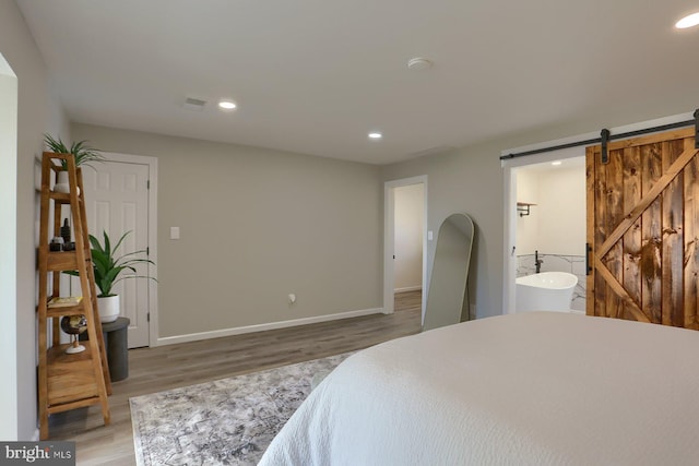 bedroom featuring connected bathroom, hardwood / wood-style flooring, and a barn door