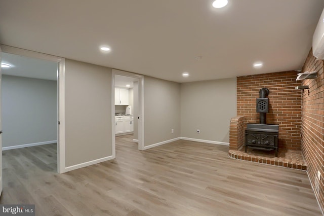 unfurnished living room featuring light hardwood / wood-style floors, brick wall, and a wood stove