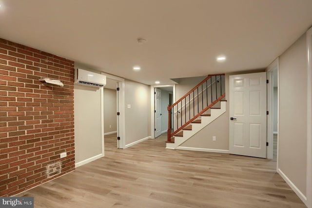 basement with an AC wall unit, brick wall, and light wood-type flooring