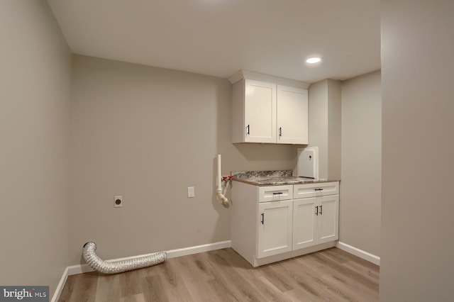 laundry area with light hardwood / wood-style floors, hookup for an electric dryer, and cabinets