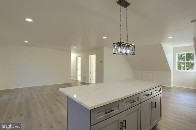 kitchen with a kitchen island, light wood-type flooring, gray cabinets, decorative light fixtures, and light stone counters