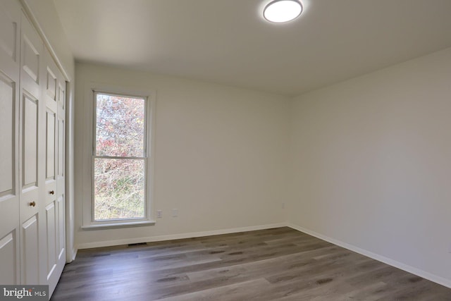 unfurnished bedroom with multiple windows, dark hardwood / wood-style floors, and a closet