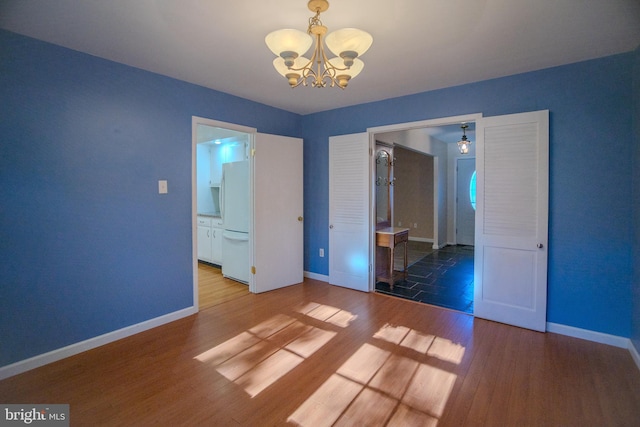 unfurnished bedroom with an inviting chandelier, hardwood / wood-style flooring, white fridge, and connected bathroom