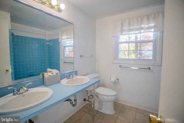 bathroom with a tile shower, double sink, toilet, and tile patterned flooring