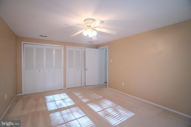 unfurnished bedroom featuring ceiling fan, light carpet, and multiple closets