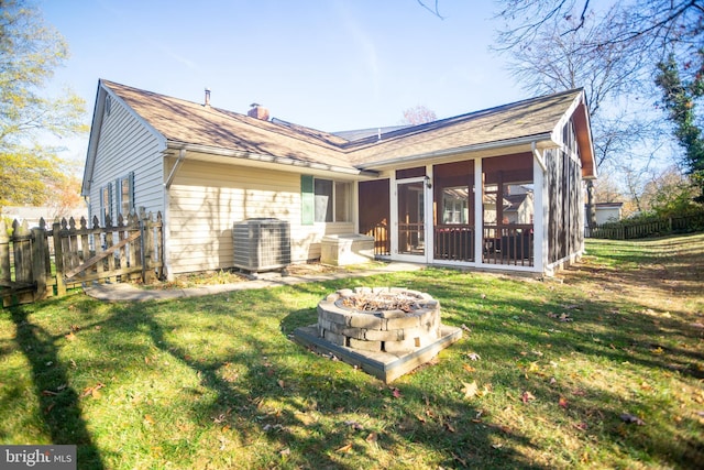 rear view of property featuring central AC, a sunroom, a lawn, and an outdoor fire pit