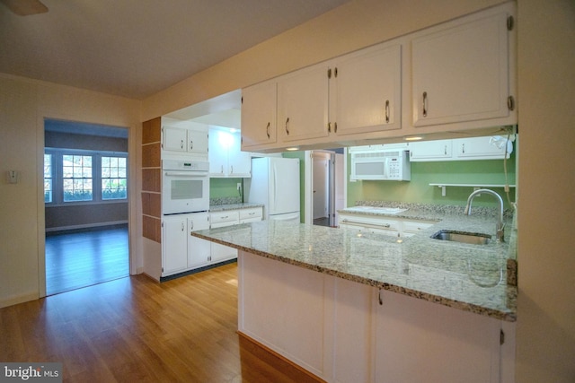 kitchen with light stone counters, kitchen peninsula, sink, white cabinetry, and white appliances