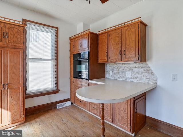 kitchen with tasteful backsplash, kitchen peninsula, light hardwood / wood-style floors, ceiling fan, and black oven