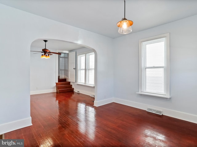 empty room featuring ceiling fan, a healthy amount of sunlight, and dark hardwood / wood-style flooring