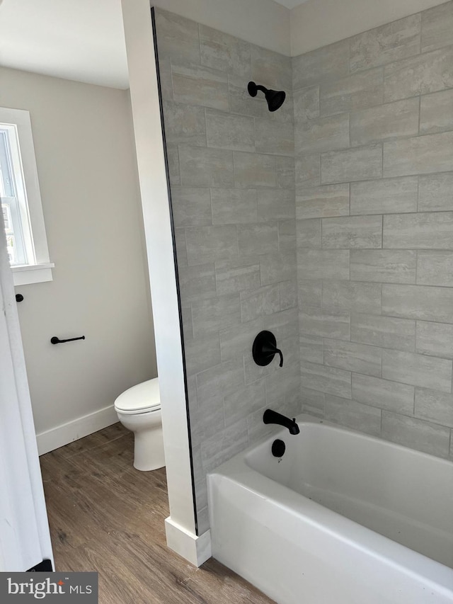 bathroom with hardwood / wood-style flooring, tiled shower / bath combo, and toilet