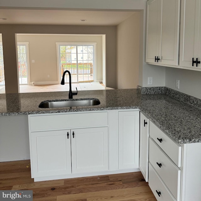 kitchen with hardwood / wood-style flooring, white cabinetry, dark stone counters, and sink