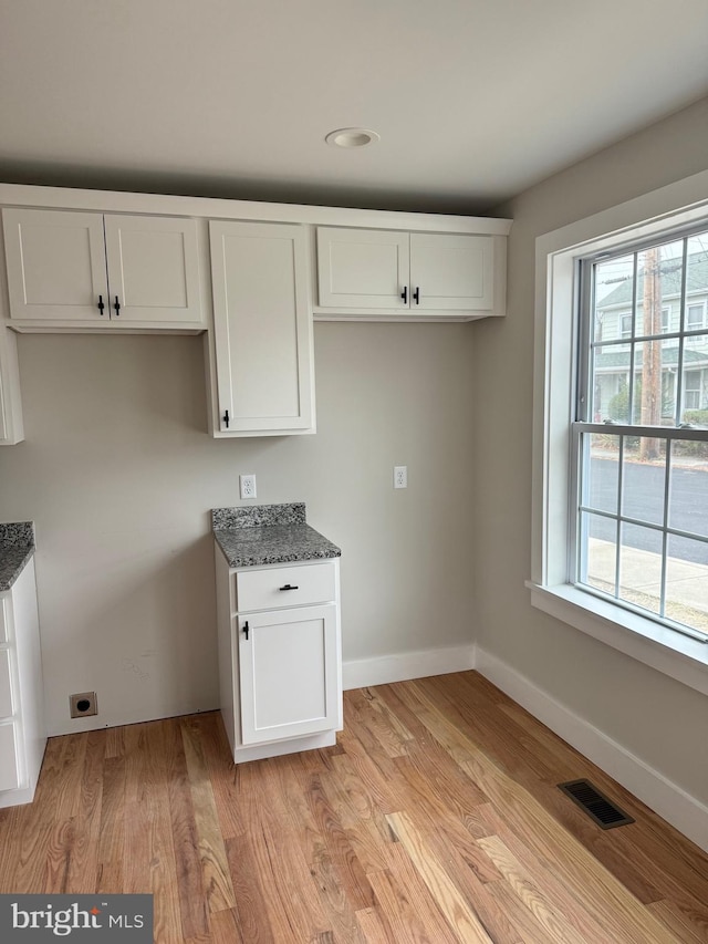 kitchen featuring white cabinetry, light hardwood / wood-style flooring, a wealth of natural light, and dark stone countertops