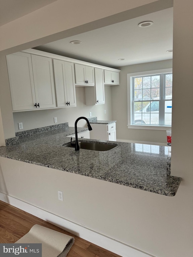 kitchen featuring stone counters, sink, dark wood-type flooring, kitchen peninsula, and white cabinets