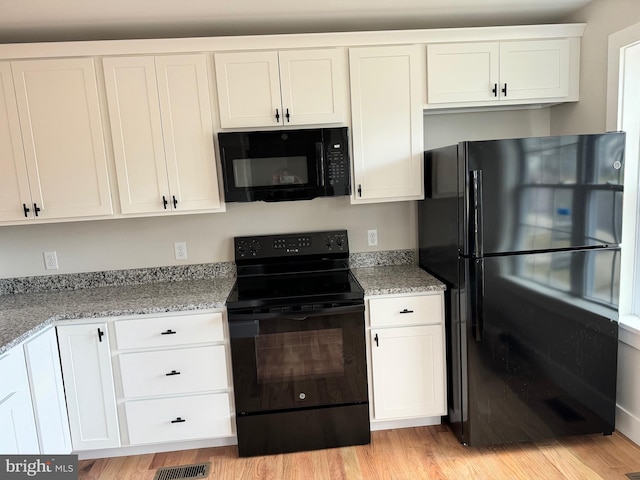 kitchen with light stone countertops, white cabinetry, black appliances, and light hardwood / wood-style floors