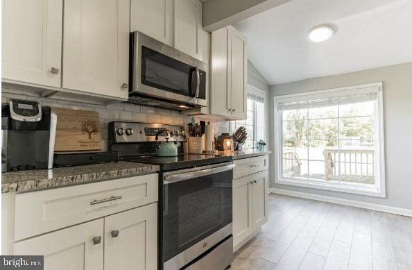 kitchen with lofted ceiling, backsplash, appliances with stainless steel finishes, white cabinetry, and light stone counters