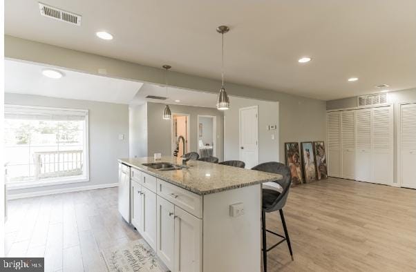 kitchen featuring light stone countertops, sink, decorative light fixtures, white cabinets, and a center island with sink