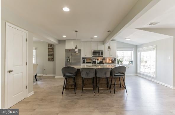 kitchen with white cabinetry, stainless steel appliances, light hardwood / wood-style floors, decorative light fixtures, and a center island