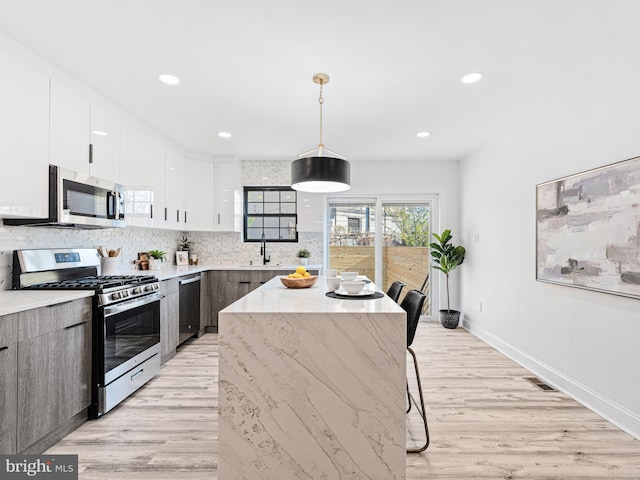 kitchen featuring hanging light fixtures, stainless steel appliances, a center island, white cabinetry, and light hardwood / wood-style floors