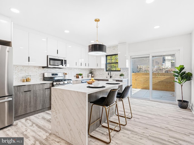 kitchen featuring a kitchen island, stainless steel appliances, pendant lighting, white cabinetry, and light hardwood / wood-style floors