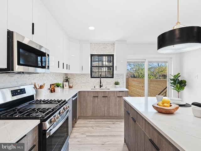 kitchen with stainless steel appliances, sink, pendant lighting, white cabinets, and light stone counters