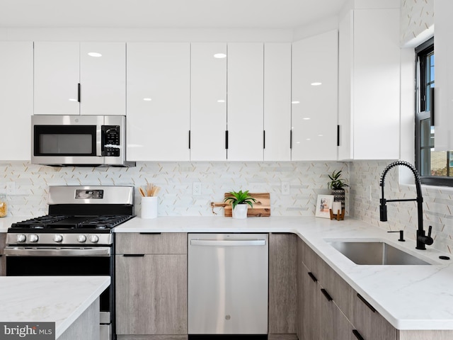 kitchen featuring decorative backsplash, sink, light stone countertops, white cabinets, and appliances with stainless steel finishes