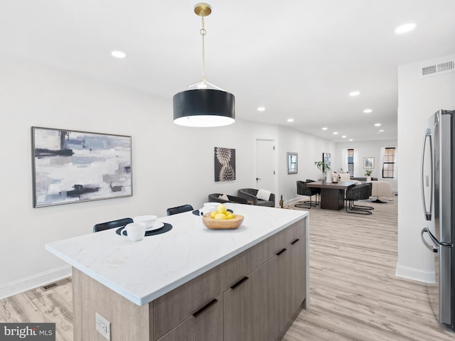 kitchen featuring hanging light fixtures, a kitchen island, a breakfast bar area, stainless steel refrigerator, and light hardwood / wood-style flooring