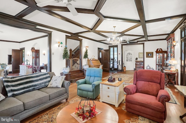 living area with coffered ceiling, beam ceiling, ceiling fan with notable chandelier, wood finished floors, and stairs