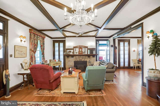 living area with wood finished floors, coffered ceiling, a stone fireplace, baseboards, and a notable chandelier