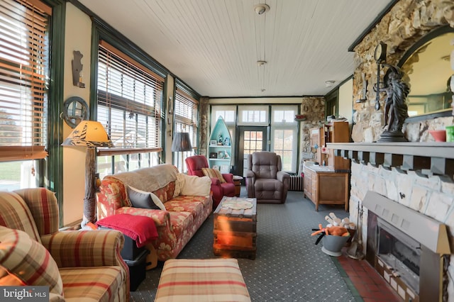 carpeted living area featuring wooden ceiling, radiator, and a stone fireplace