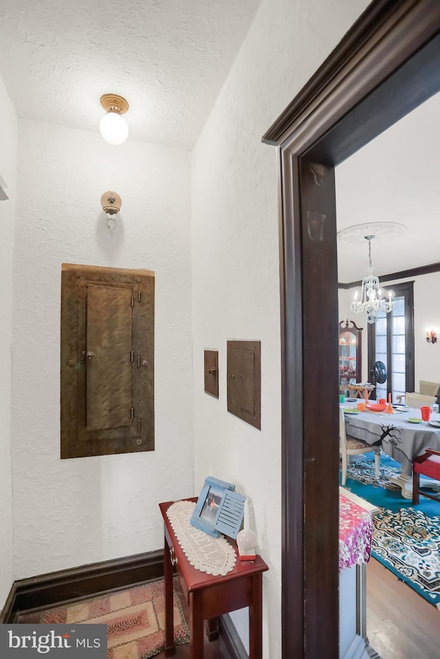 hall featuring a textured ceiling, a textured wall, wood finished floors, and a chandelier