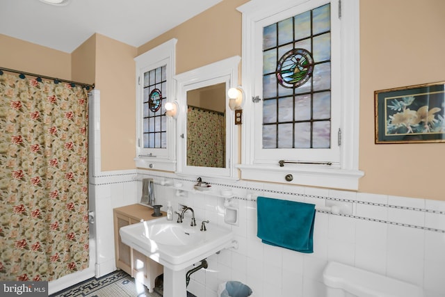 full bathroom featuring a wainscoted wall, tile walls, a sink, and a shower with shower curtain