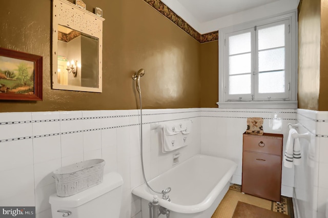 bathroom featuring tile walls, a wainscoted wall, toilet, and a bathing tub