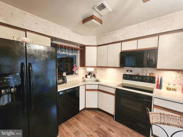 kitchen featuring light hardwood / wood-style flooring, white cabinets, black appliances, and sink