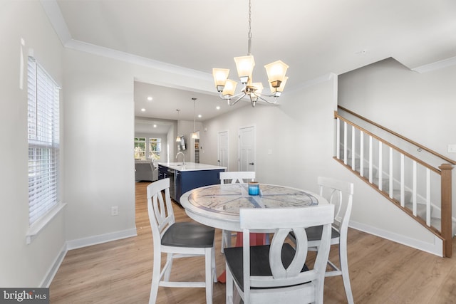 dining room featuring sink, ornamental molding, a chandelier, and light wood-type flooring